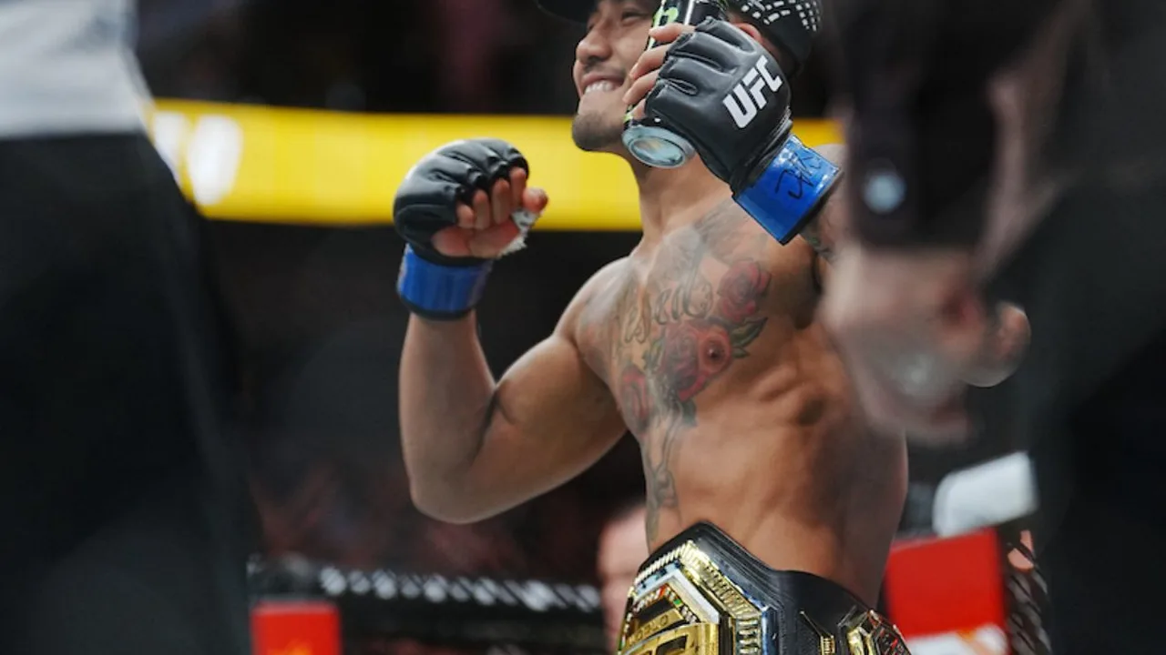 Octógono do UFC vazio com cinturão peso-mosca em destaque sobre a tela central durante evento