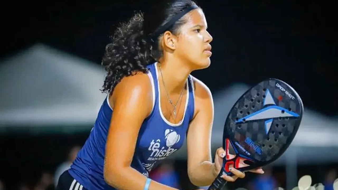 Tenista juvenil brasileira em ação durante partida em quadra de saibro, executando backhand cruzado com precisão técnica
