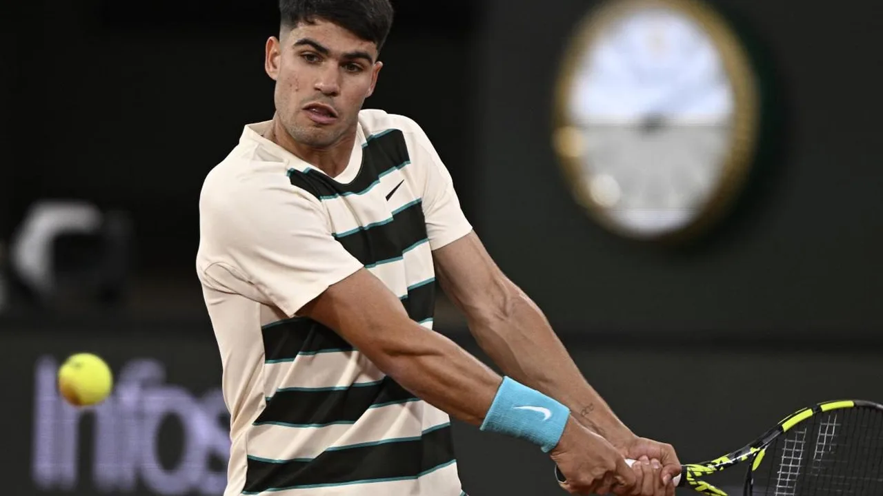 Carlos Alcaraz segurando troféu de Roland Garros com expressão preocupada, quadra de saibro ao fundo