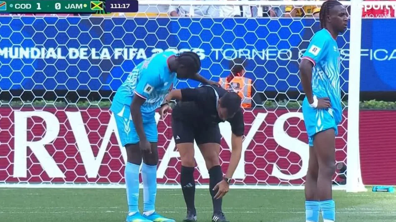 Árbitro em campo durante partida internacional segurando cartão, com brasão da Fifa em fundo desfocado