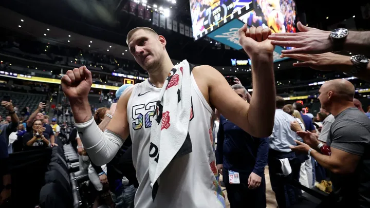 Jogador de basquete da NBA distribuindo assistência enquanto adversários tentam rebote na quadra