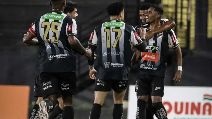 Atacante comemorando hat-trick em estádio lotado, segurando a bola com as duas mãos acima da cabeça