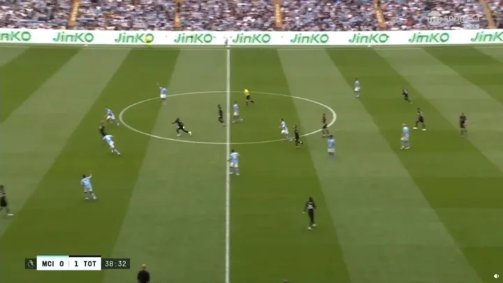 Árbitro assistente levantando a bandeira de offside em partida de futebol, com jogadores em campo ao fundo