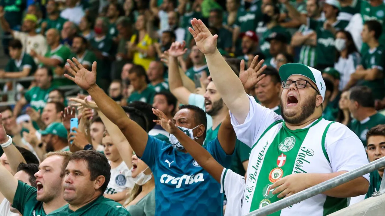 Leila Pereira em evento do Palmeiras com expressão séria, ao fundo o escudo do clube alviverde