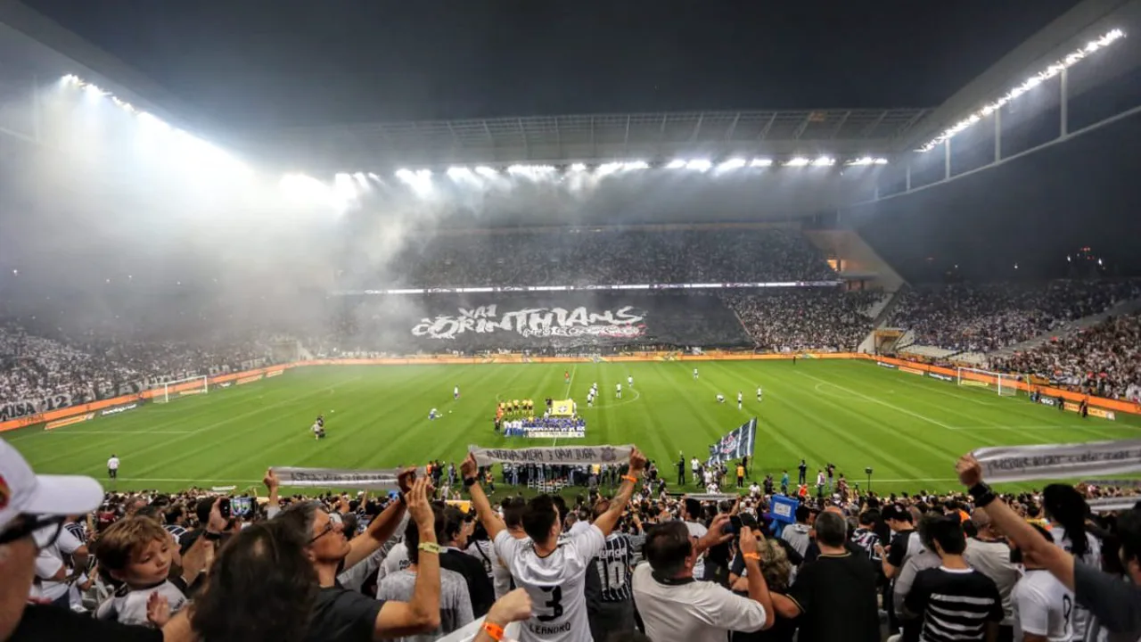 Estádio do Corinthians com torcida nas arquibancadas e jogadores em campo durante partida do Brasileirão 2026