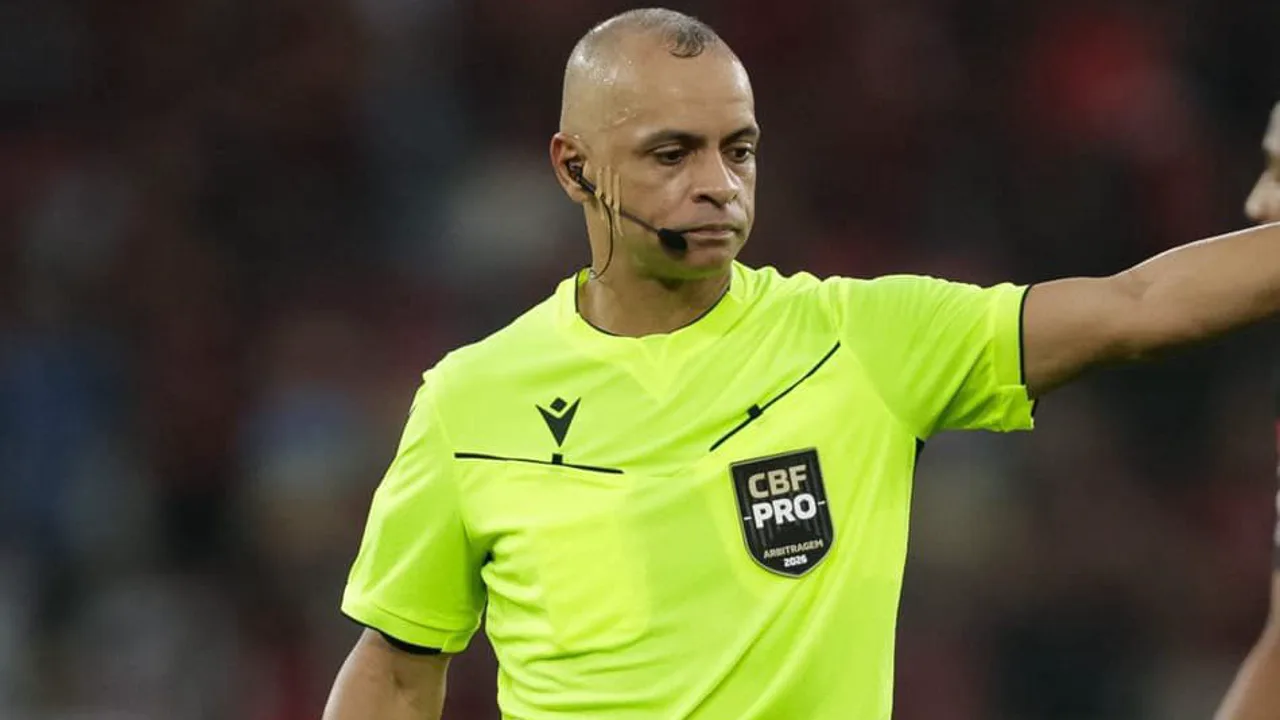 Árbitro Wilton Pereira Sampaio apitando partida de futebol com jogadores ao fundo em estádio lotado