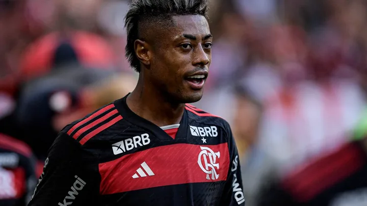 Bruno Henrique comemorando gol pelo Flamengo ao lado de Jérémy Doku em ação pelo Manchester City na Champions League