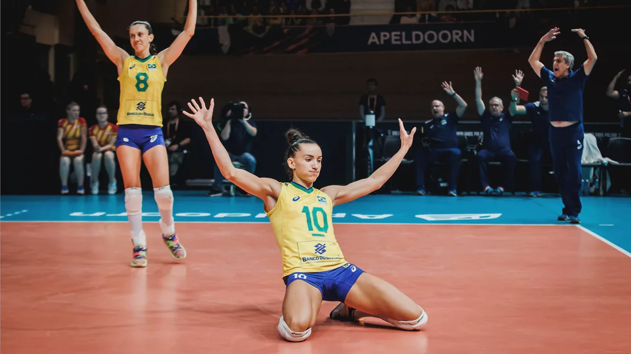 Jogadoras de vôlei em quadra durante o tie-break, com placar acirrado no telão do ginásio